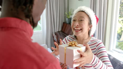 happy, excited diverse couple exchanging christmas gift and embracing at home, slow motion