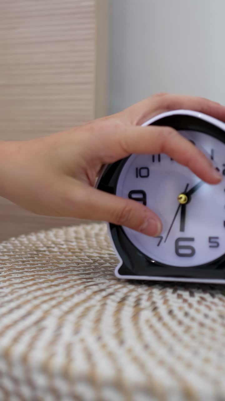Una mano si allunga per spegnere una sveglia nera su un comodino.