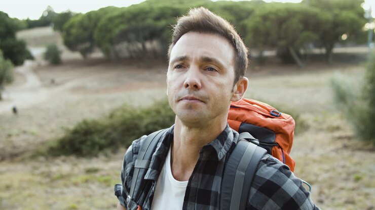 Portrait of pensive trekking guy wearing backpack outdoors
