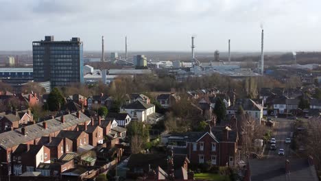 Aerial-view-over-park-trees-to-industrial-townscape-with-blue-skyscraper,-Merseyside,-England,-Zoom-in-shot