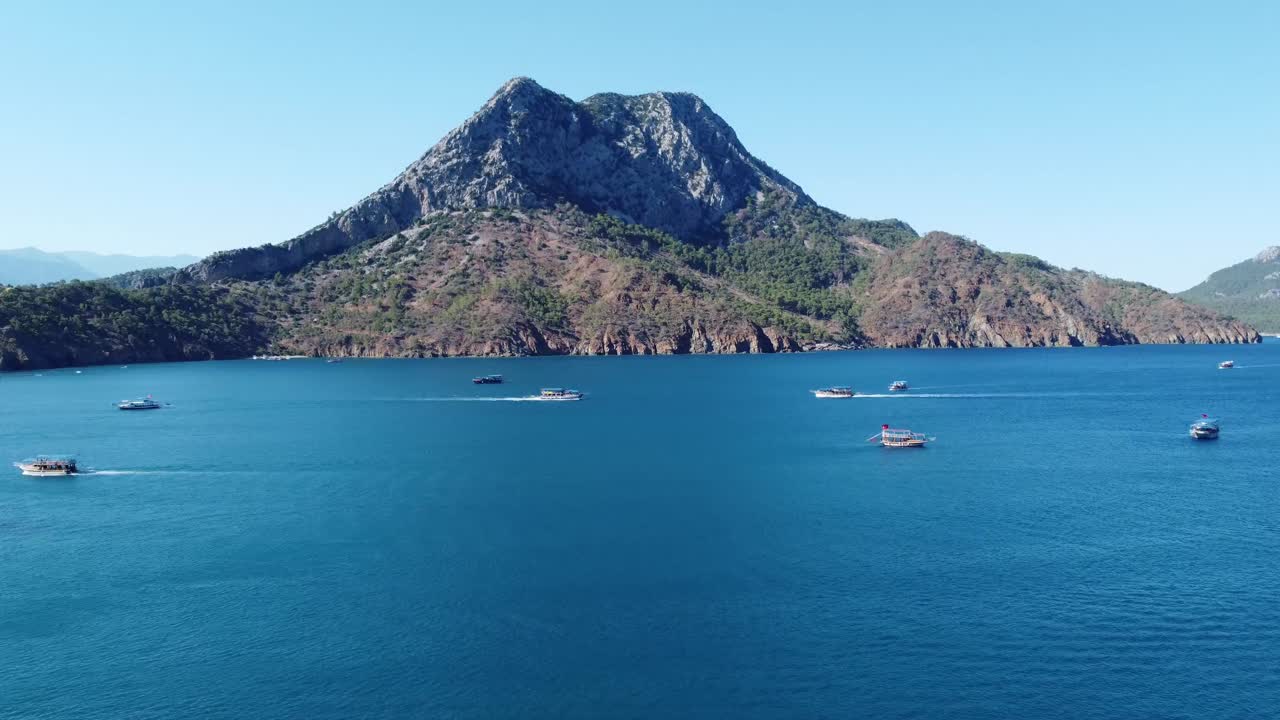 Aerial drone view showing rugged mountainous island near Kekova surrounded by deep blue sea with moving boats, perfect for Social Media travel content and scenic coastal landscape scenes