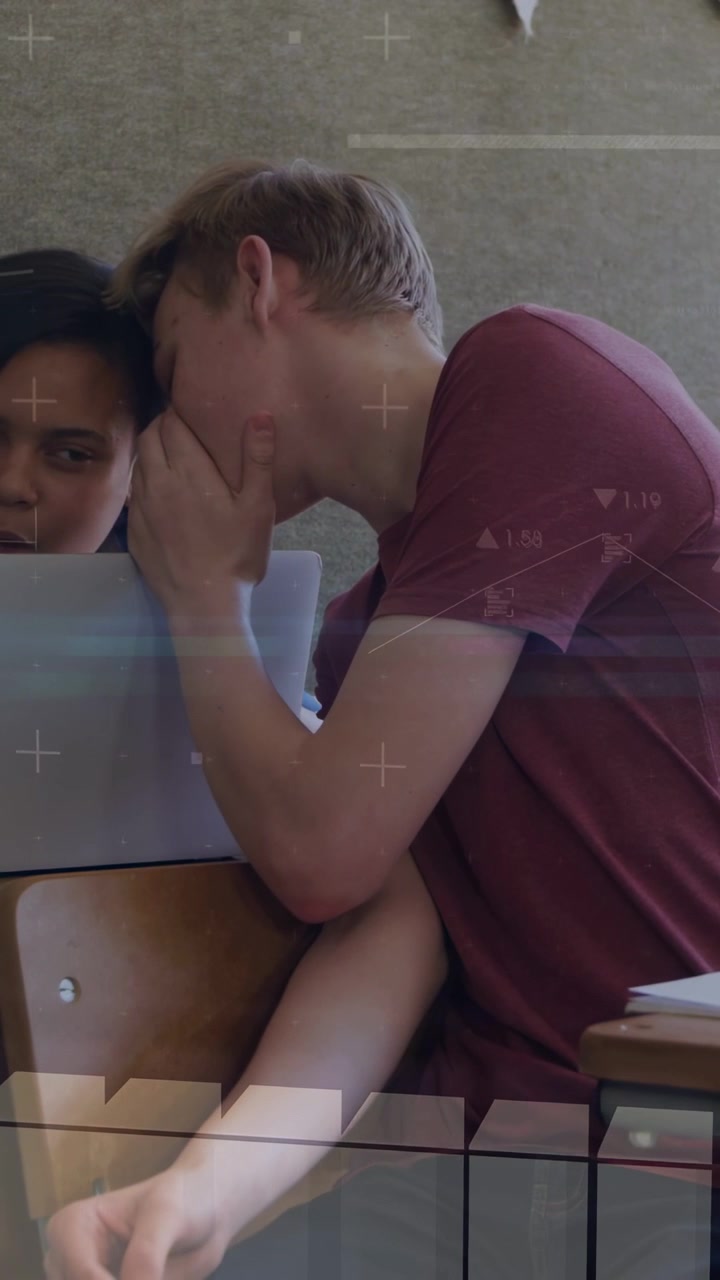 Video verticale: Adolescente maschio appoggiato, mano vicino alla bocca, che sussurra e condivide appunti di studio sul laptop.