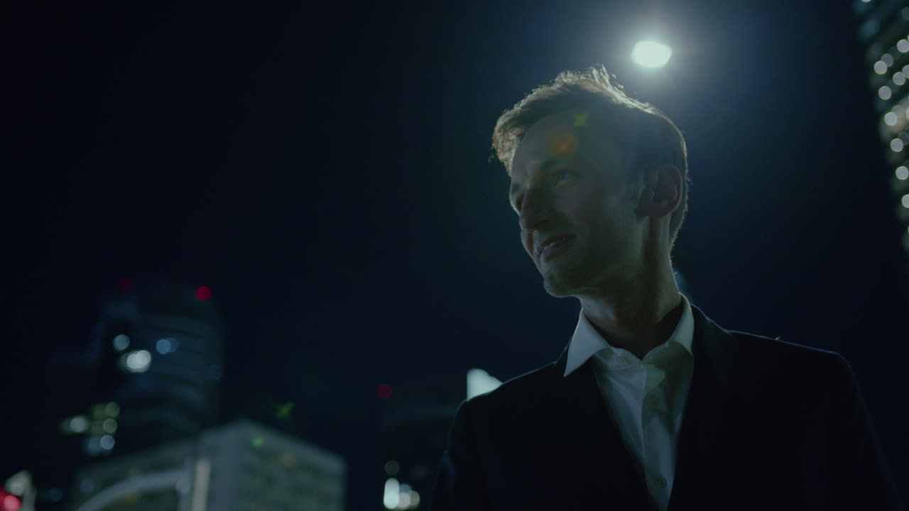 자신감 넘치는 젊은 사업가, 밤에는 시내에서, 금융 시내 중심의 불빛이 그의 자랑스러운 몸짓에 불타고 있습니다.