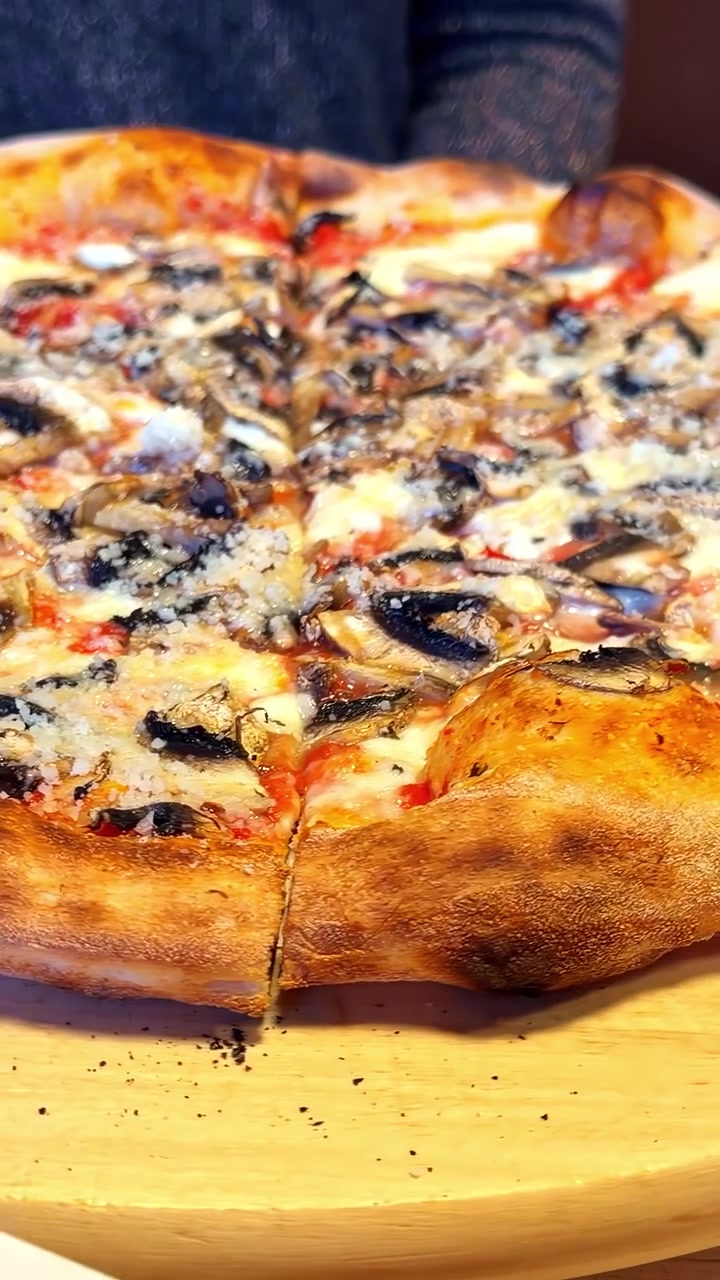 Pizza ai peperoni e mozzarella e pizza ai funghi che girano su un tagliere di legno rotante con crosta dorata, primo piano.