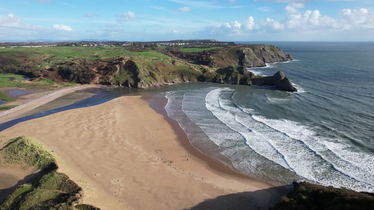 Beach and surf at Three Cliffs Bay in Wales revealed from low altitude as a drone flies backward and tilts upward toward the cliffs