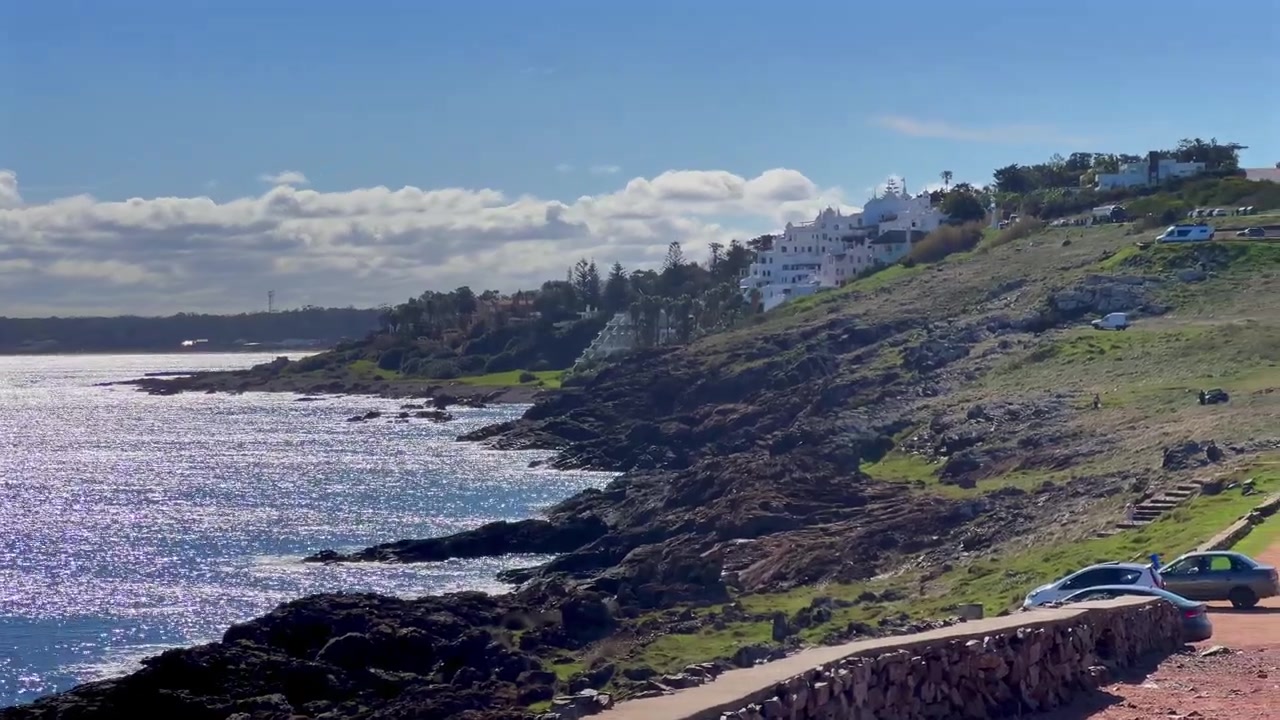 Punta Ballena, panorâmica lateral da costa rochosa com a encosta de Casapueblo e a água cintilante do oceano.