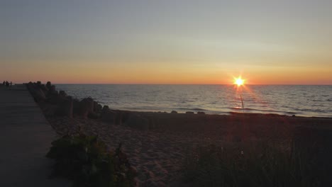 Time-lapse-of-beautiful-scenic-beach-view-at-sunset-with-silhouettes-of-people-taking-photos-at-the-seaside-near-the-Karosta-North-Pier,-wide-shot