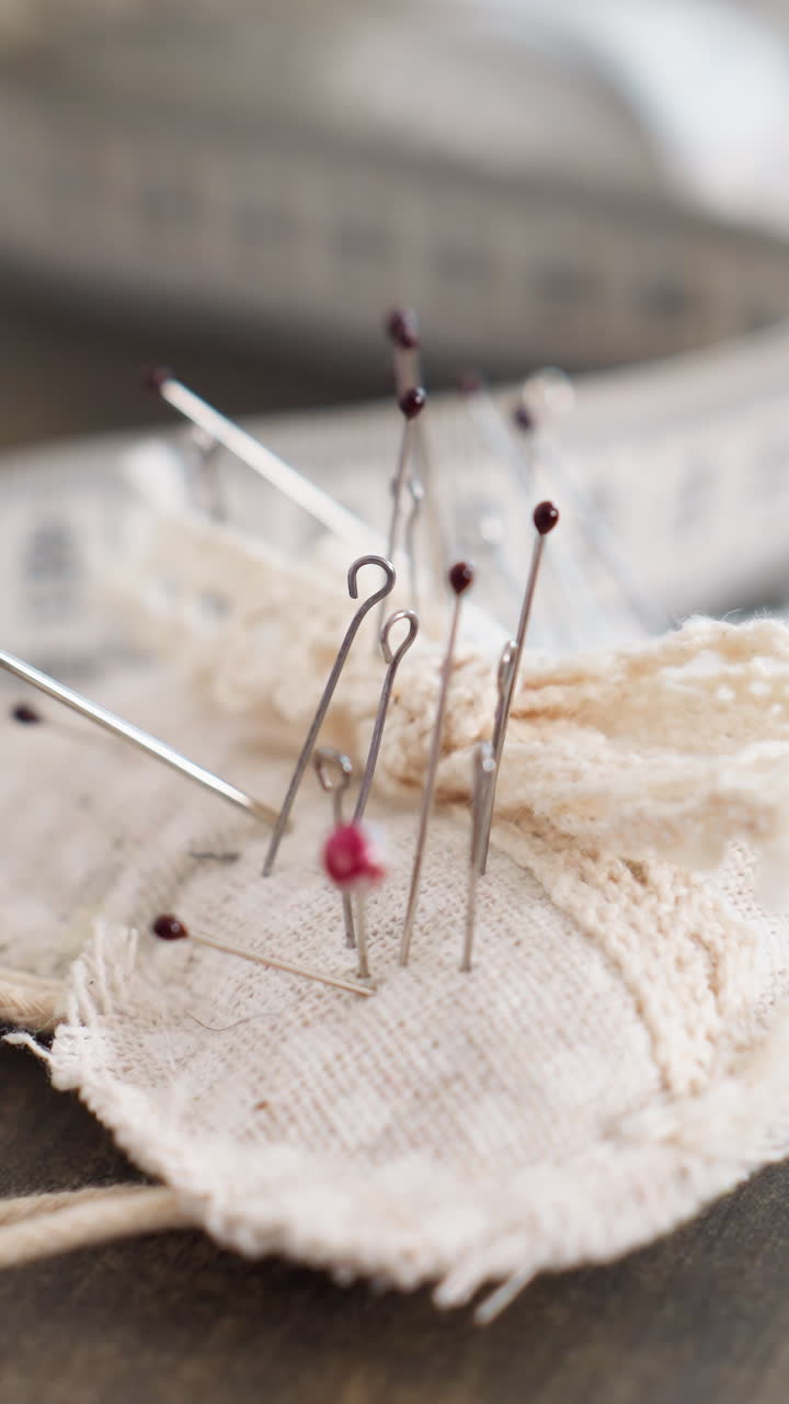 closeup pincushion with pins and needles, linen pad texture in sharp focus, measuring tape blurred in background, delicate pinheads and metal shafts, intimate craft moment for precision sewing