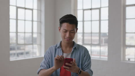 Retrato-De-Un-Joven-Estudiante-Asiático-Enviando-Mensajes-De-Texto-Navegando-Por-Las-Redes-Sociales-Usando-Tecnología-Móvil-De-Teléfono-Inteligente-En-El-Fondo-De-Las-Ventanas-De-Una-Habitación-De-Apartamento-Vacía