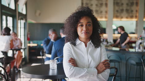 portrait of female manager of busy cocktail bar in restaurant with customers smiling at camera