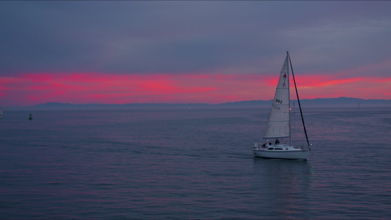 velero en el océano con puesta de sol rosa y naranja mirando hacia el horizonte con montañas de la isla