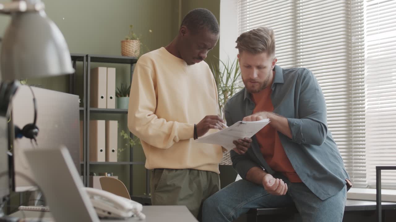 Two Diverse Male Colleagues Discussing Business Documents in Office