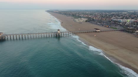 4k ariel drone shot heading straight down the pier in california, surf city usa as a military troop trains, surfers catch waves, a lifeguard truck drives by and families enjoy summer vacation