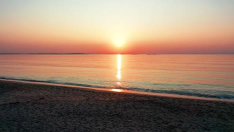 View-of-Ocean-Sunrise-While-Waling-on-Beach-with-Bright-Glowing-Sun-Casting-Colorful-Red,-Orange,-Purple,-and-Yellow-Reflections-Over-Peaceful-Rippling-Waves-of-the-Sea-with-Beautiful-Sky