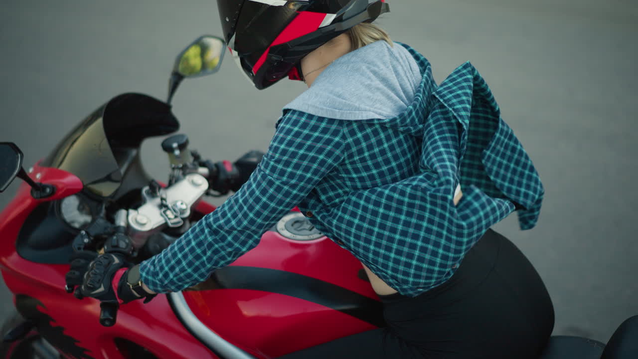 한 여성이 빨간색 파워 자전거를 타고 부드럽고 타르로 된 도로를 따라, 그녀의 체크 된 셔츠가 바람에 날아다니며, 그녀가 앞으로 기울어지면서 몸통의 일부를 노출시니다.
