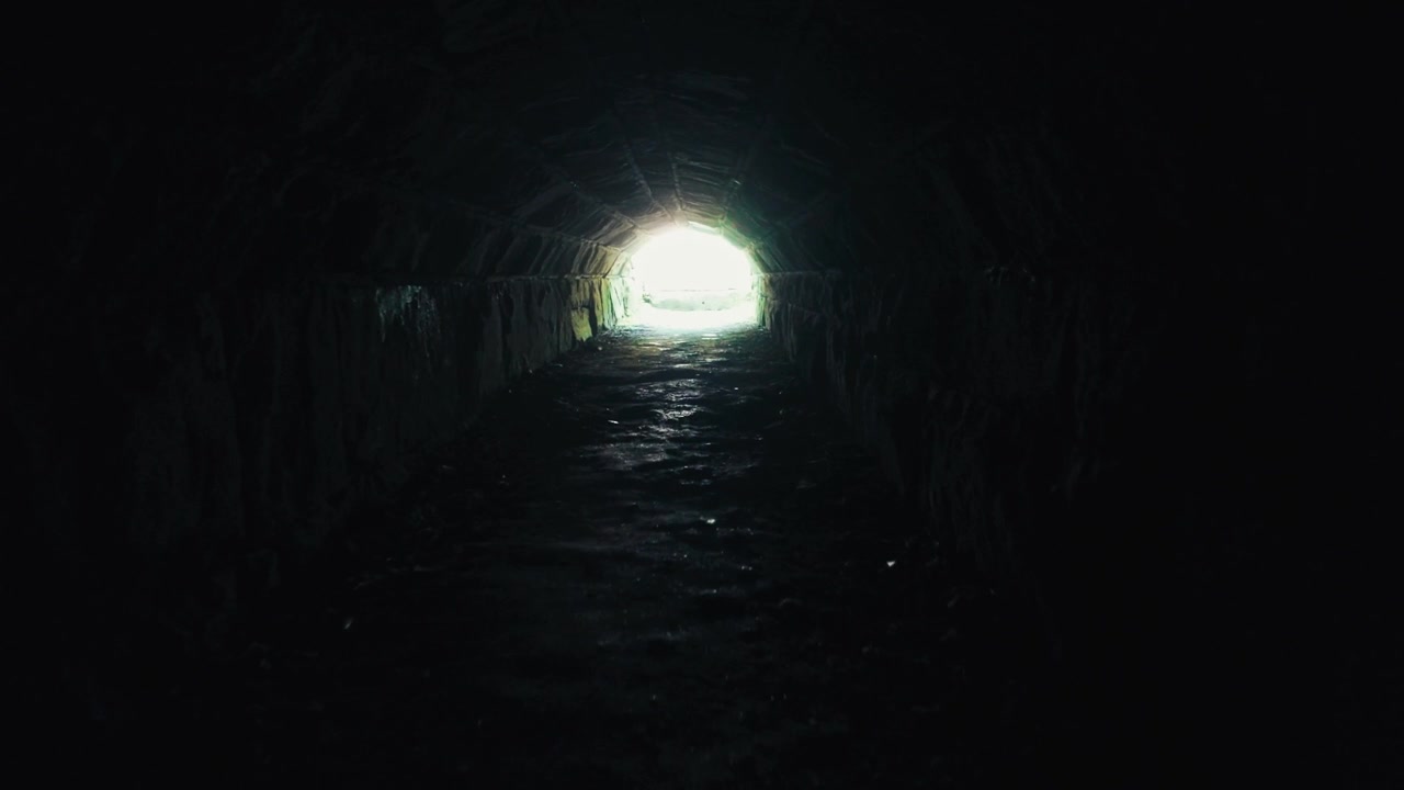 A moving shot through a dark tunnel, moving toward a bright light at the end.