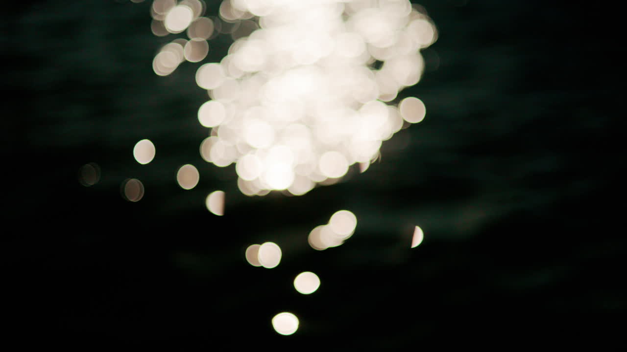 Shimmering sunlight reflects on gentle sea waves, creating bright sparkling bokeh on a deep blue water surface