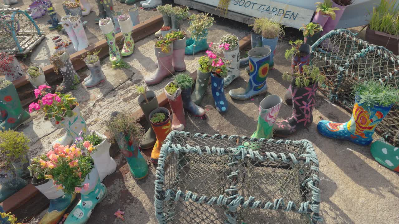 Decorative painted boots filled with plants displayed next to fishing gear on a sunlit concrete floor
