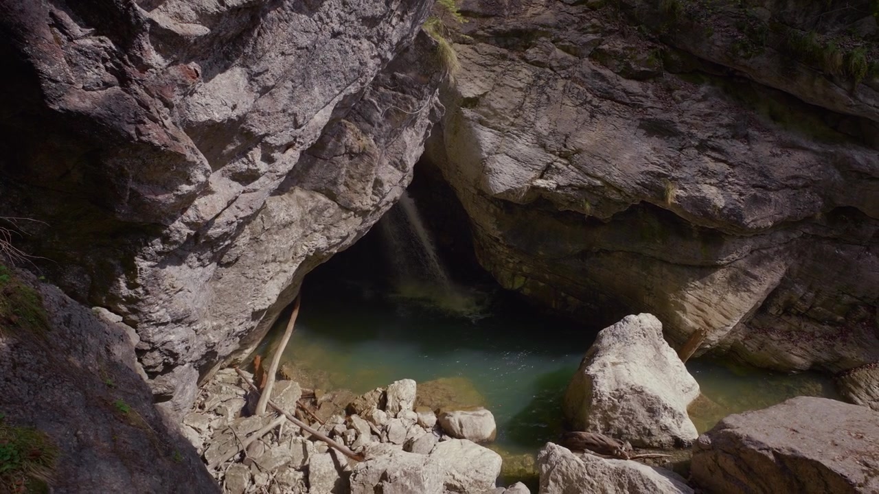 Cascata che si getta dal soffitto di una grotta rocciosa in una piscina turchese, al rallentatore. Gola di Starzlachklamm.