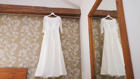 top of a wedding dress hanging from the four-poster bed, in the room where the bride is getting ready for her wedding