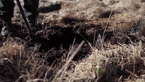 farmer in boots digging soil on grassy field with shovel