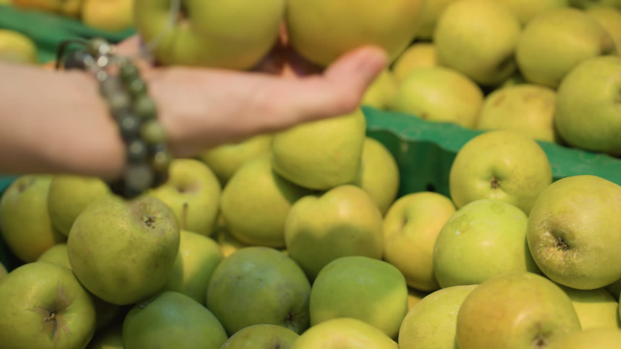 매장 상점의 상자에서 두 개의 사과를 집어 들고 있는 드 브래슬을 착용한 손의 모습. 드 헬드 카메라로 앞면에서 찍은 사진