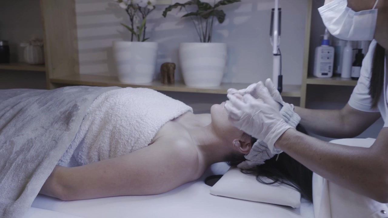 Mani guantate massaggiano delicatamente la fronte del cliente in una rilassante routine viso.