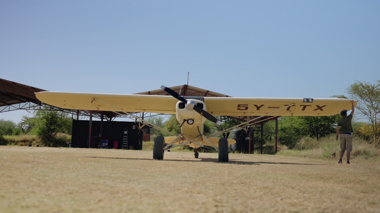Uomo che ispeziona l'ala di un piccolo aereo su una pista d'atterraggio erbosa