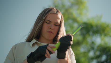 joven adulto con cabello rubio luchando para ajustar la boquilla de la bomba de aire verde mientras está de pie al aire libre en un día soleado, el fondo cuenta con árboles verdes exuberantes