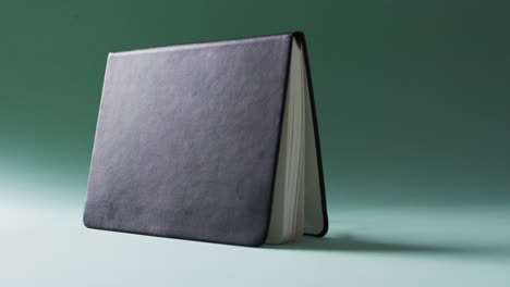 Close-up-of-open-black-book-standing-horizontal-with-copy-space-on-green-background-in-slow-motion