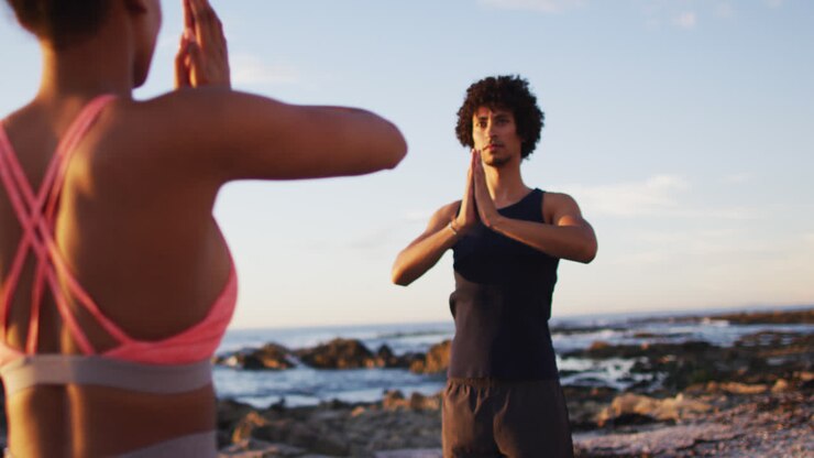 Coppia afroamericana che pratica yoga insieme sulle rocce vicino al mare.