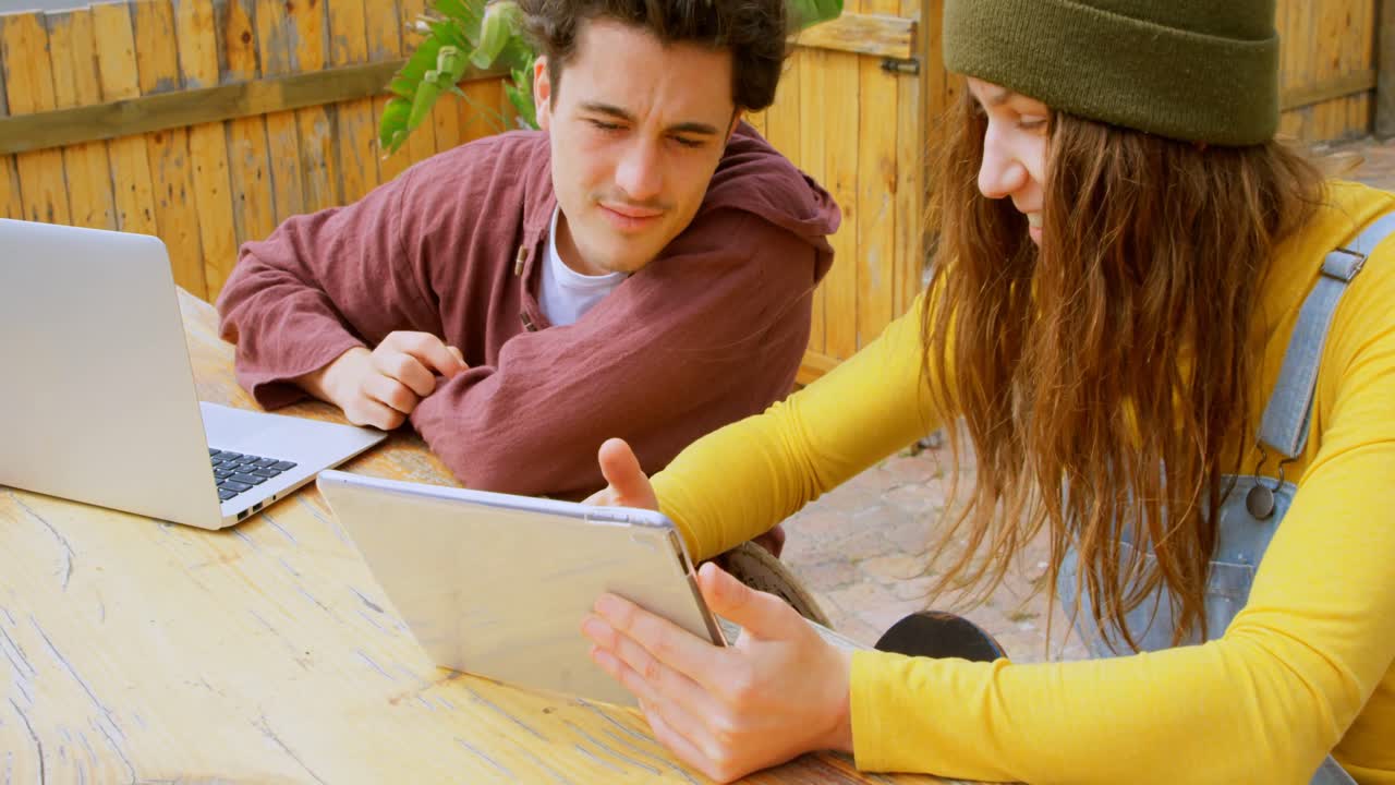 vista frontal de jóvenes skateboarders caucásicos discutiendo en una tableta digital en un café al aire libre 4k