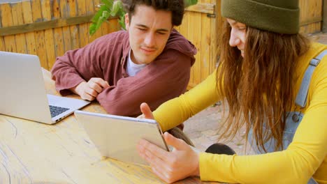 Front-view-of-cool-young-caucasian-skateboarders-discussing-on-digital-tablet-at-outdoor-cafe-4k