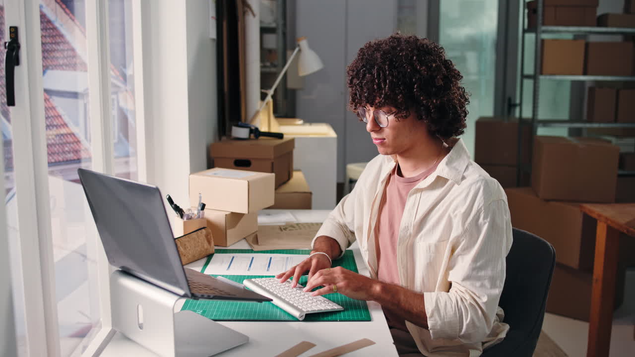 Young Man with Curly Hair Working on Laptop in Office