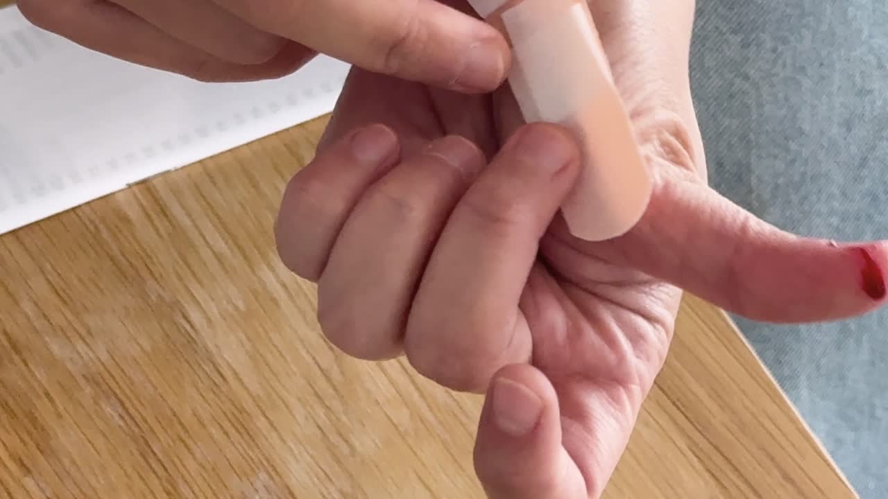 Close-up of hands applying a bandage to a bleeding finger on a wooden table with natural lighting