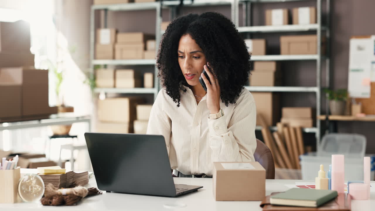 Donna d'affari stressata al telefono che lavora al laptop in un ufficio magazzino