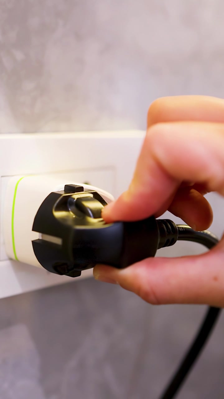 Close-up shot of a hand removing a black electrical plug from a white wall adapter