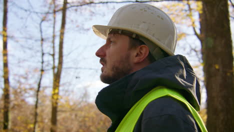 fotografía en primer plano de la cara de un trabajador que lleva un casco y un chaleco de seguridad en el medio del bosque, de mano