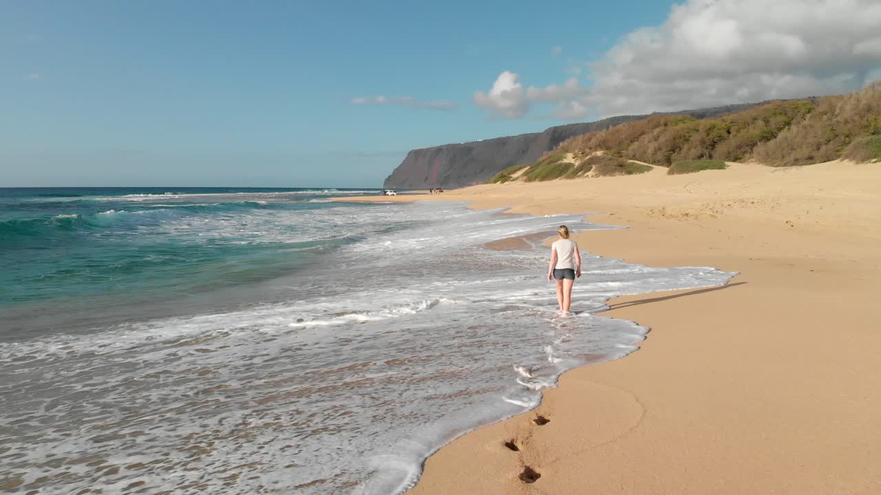 Version One. Low Aerial Tracking Shot of Girl Walking on Golden Secluded Beach in Hawaii, with Footprints in the Sand.