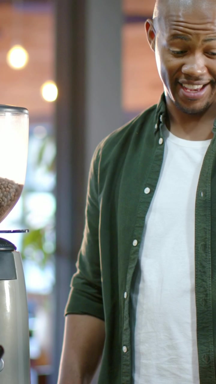 Video verticale: Uomo che parla con camicia verde ordina al bancone del caffè, barista che usa il macinacaffè