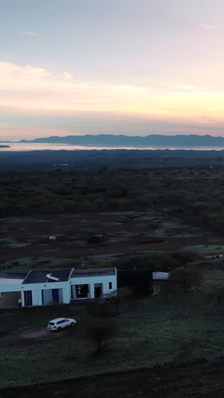 Solnedgang over afsidesliggende bondegård i kratland med fjerne bjerge, blødt gyldent lys, fejende panorama-luftoptagelse. Medie