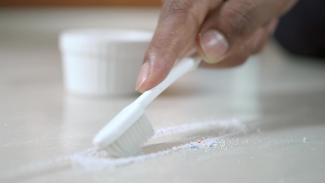 Person Cleaning Tile Grout with Toothbrush and Powder