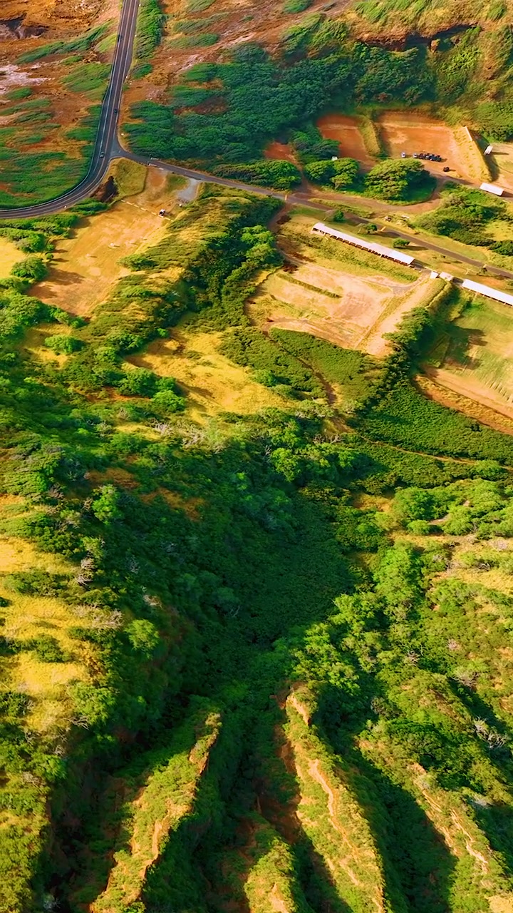 Vista aerea dall'alto di un pendio vulcanico profondamente scanalato con canali di erosione paralleli, campi agricoli pianeggianti e strada in cima. Video verticale