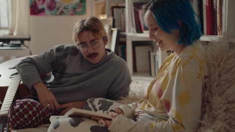 man with guitar lying on bed and discussing book with girlfriend