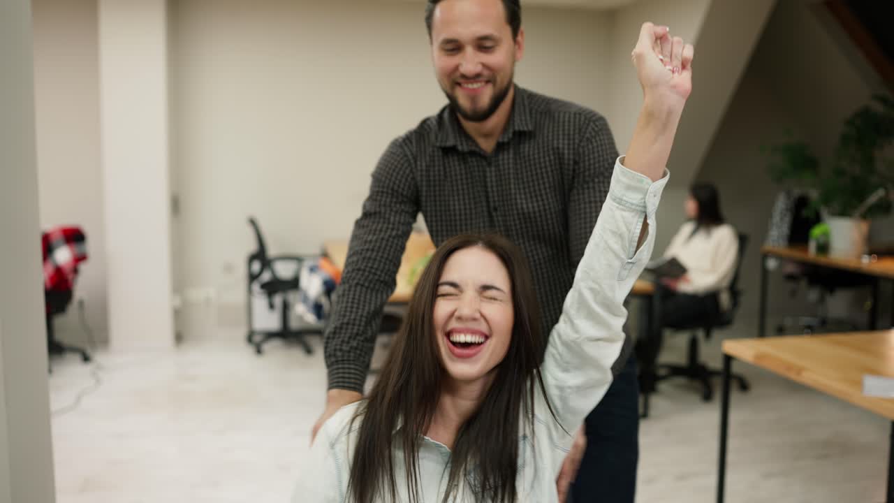 compañeros alegres que se divierten emocionados montando en una silla de oficina en el espacio de coworking