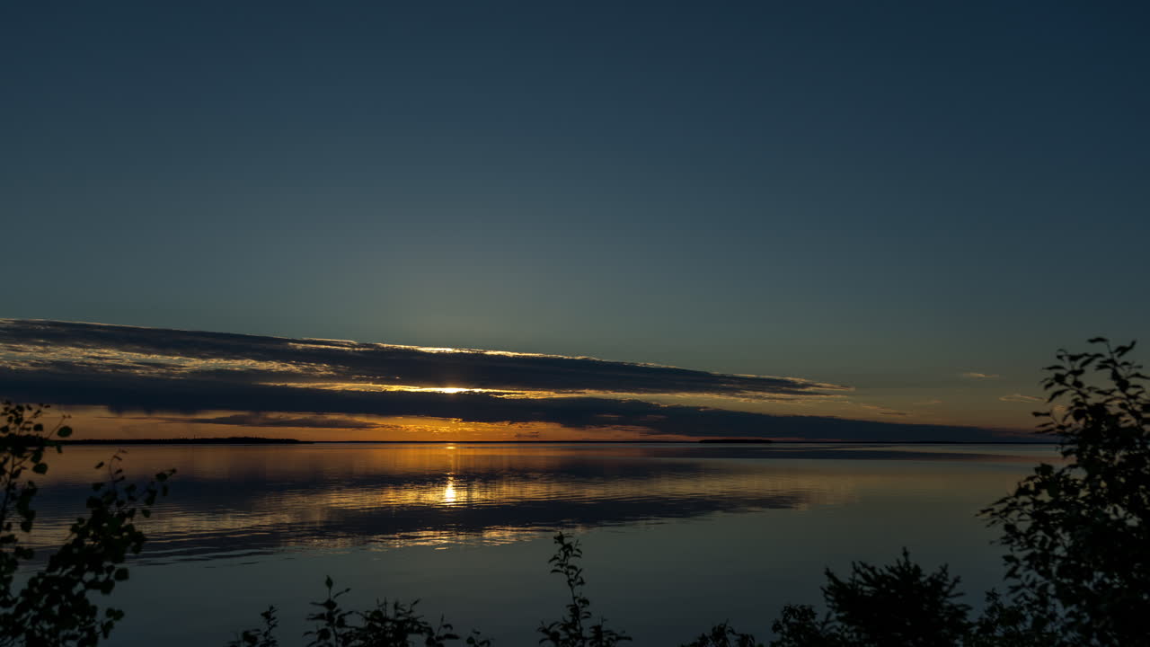 태양이 지평선 아래로 사라지기 전에 구름이 굴러오는 동안 조용한 물 위에서 아름다운 일몰의 타임 스 뷰