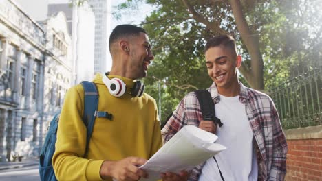 Two-happy-mixed-race-male-friends-walking-and-using-map-in-the-street