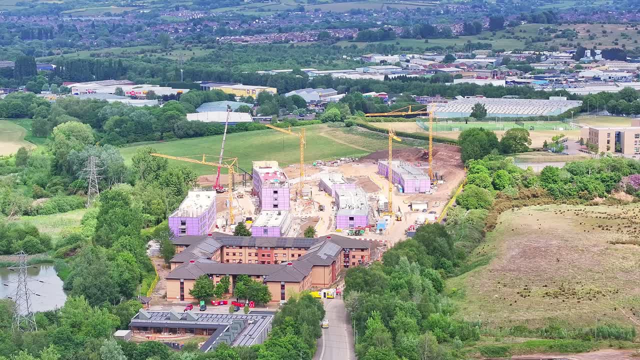 Aerial view of new residential complexes under active construction near Stoke, surrounded by lush greenery and small housing, suburban out-of-city area, daytime, England
