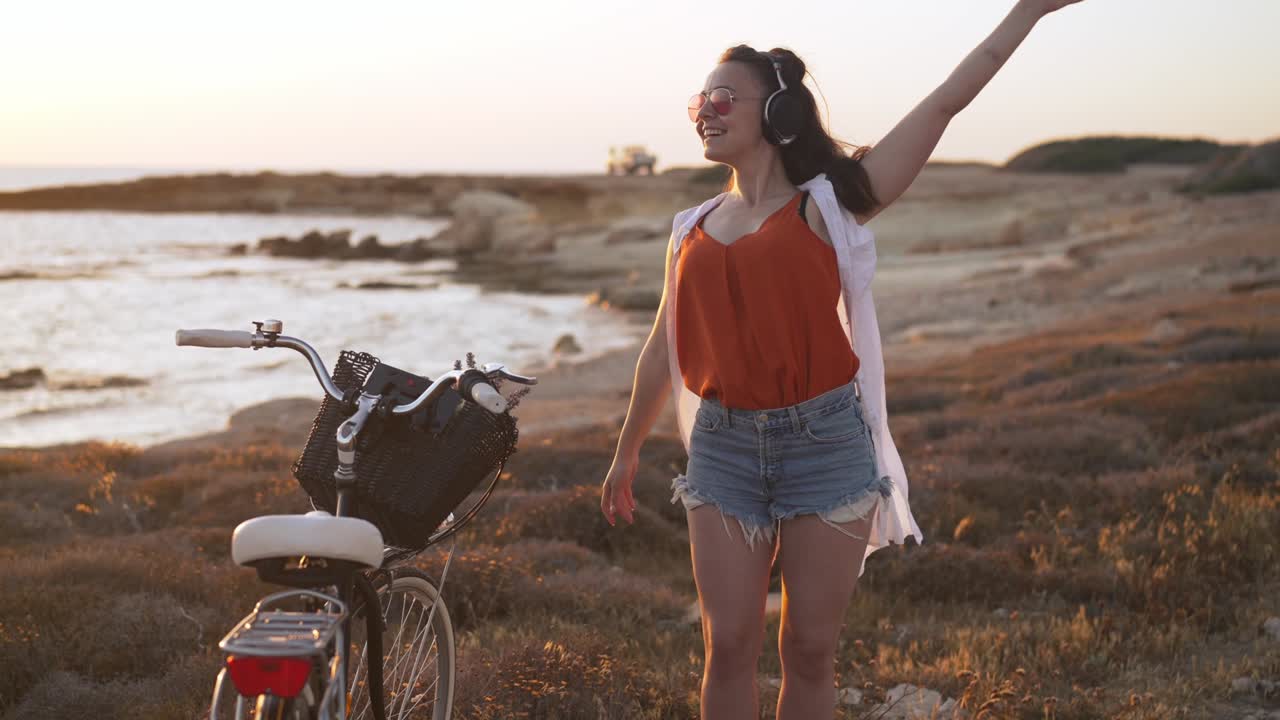 Portrait of happy excited carefree woman in headphones dancing in slow motion on Mediterranean sea beach smiling. Joyful Caucasian tourist listening to music enjoying hobby on vacations on Cyprus.
