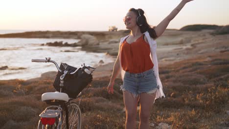 portrait of happy excited carefree woman in headphones dancing in slow motion on mediterranean sea beach smiling. joyful caucasian tourist listening to music enjoying hobby on vacations on cyprus.